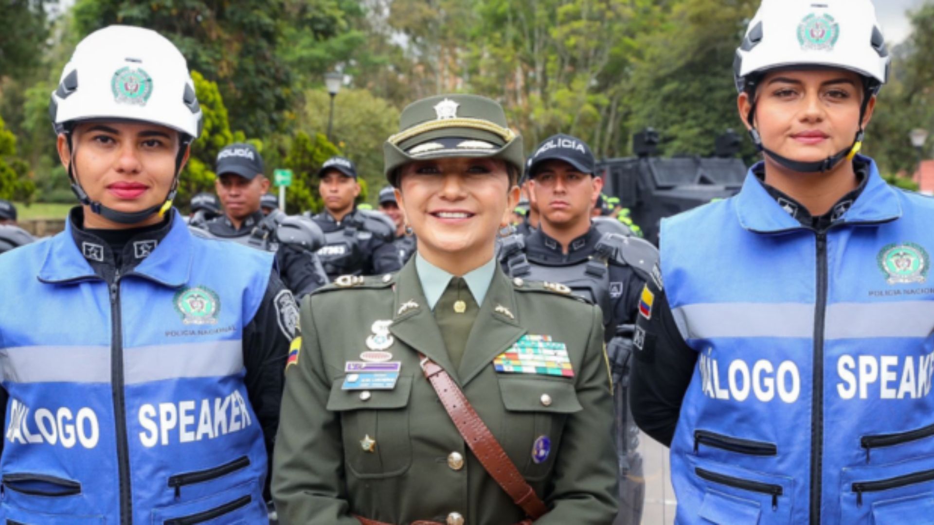 Mujer vestida de policía en el centro con dos mujeres con chalecos azules y cascos blancos a los lados