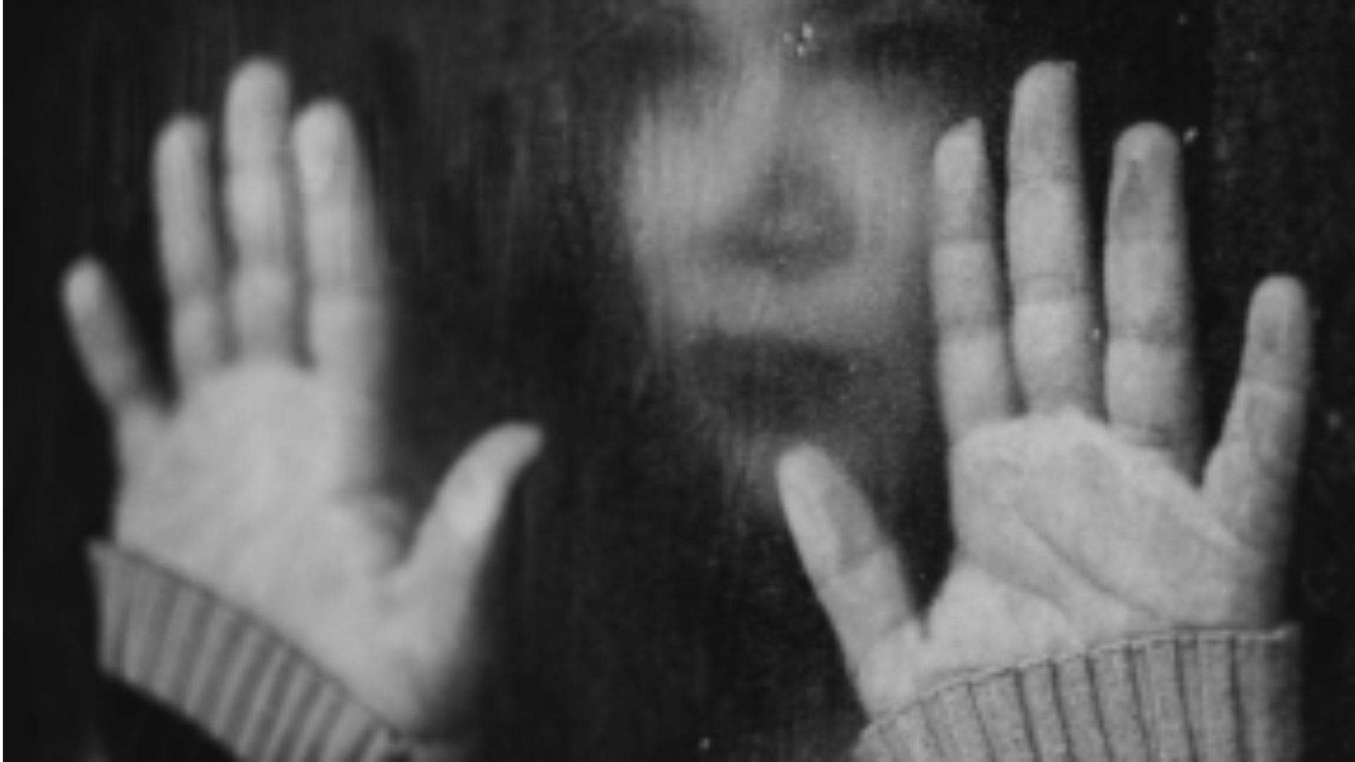 Mujer con las manos frente a una ventana empapada en blanco y negro