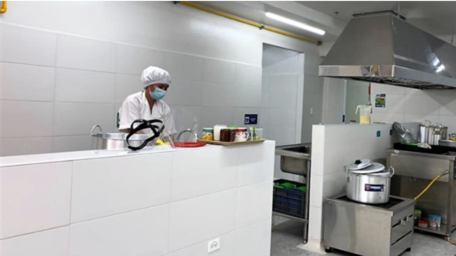 Mujer vestida con traje de cocinera al lado de una estufa de un comedor comunitario