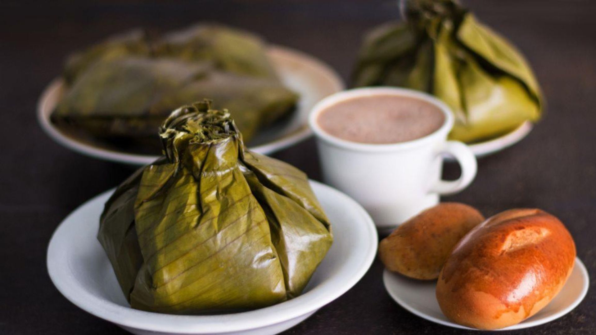 Plato de tamal con un pocillo de chocolate y pan al lado