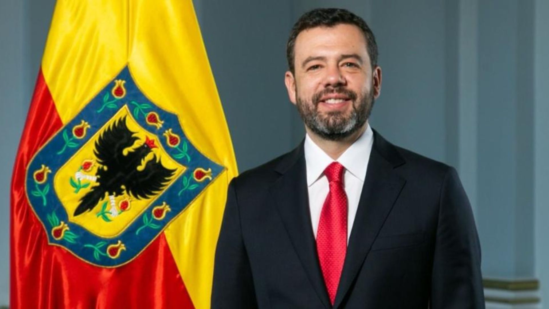 Foto del alcalde Carlos Fernando Galán con traje negro, delate de una bandera de Bogotá