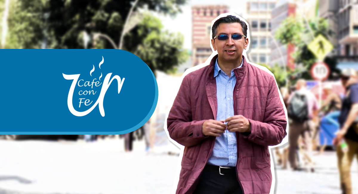 Hombre en plano americano con gafas oscuras, camisa azul claro, chaqueta vinotinto y pantalón negro