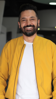 Óscar Julián Gómez-productor, hombre en plano medio con camiseta blanca y chaqueta amarilla