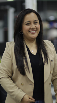 Alejandra Silva- Productora, mujer con pelo largo y suelto con blusa negra y blazer caqui.