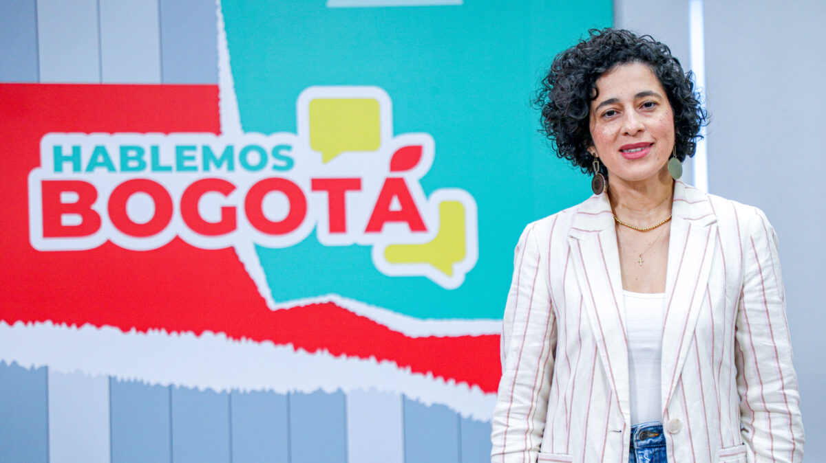 Magda Páez Torres, en el set de Hablemos Bogotá, con una chaqueda de lineas verticales blanca y rosadas.