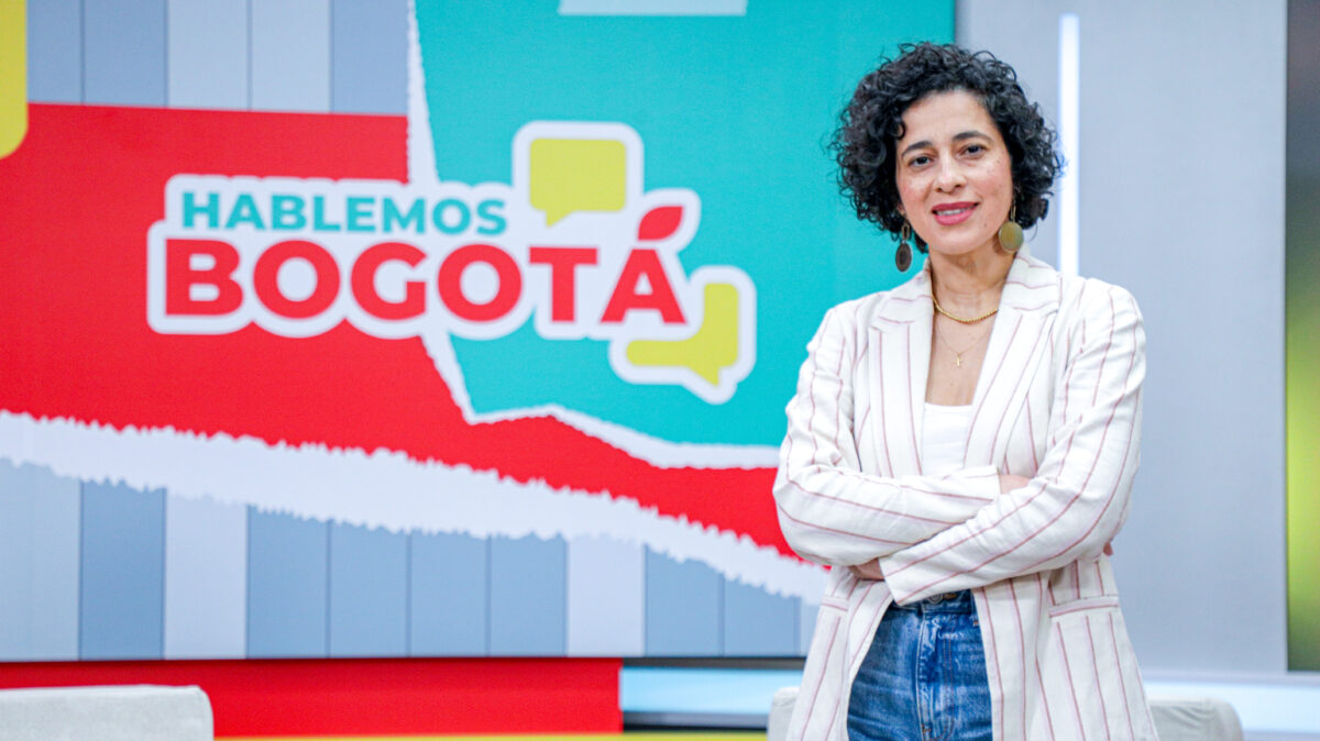 Magda Páez Torres, en el set de Hablemos Bogotá, con una chaqueda de lineas verticales blanca y rosadas.