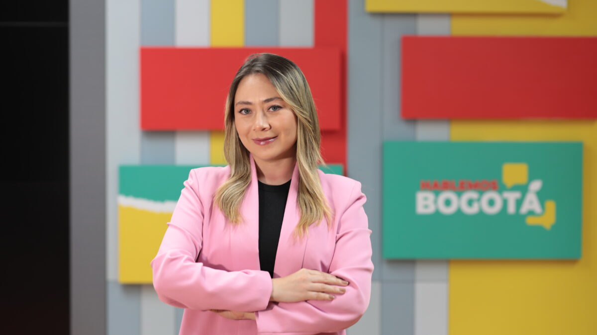 Yuri Paola Rodríguez Meneses, periodista, vestida de camisa negra y blazer palo de rosa con los brazos cruzados, en el set de Hablemos Bogotá.