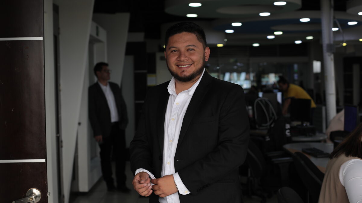 Alexander Vera, periodista de AHORA, vestido con traje negro, camisa blanca y en la redacción de Canal Capital.