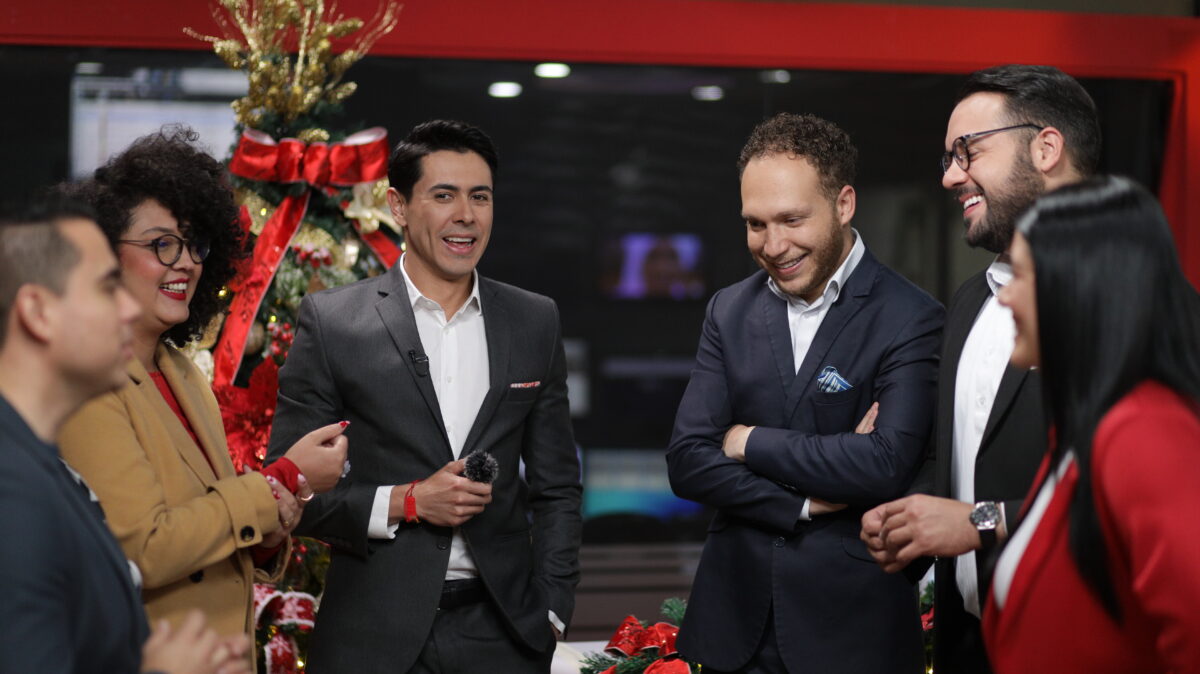 Jenny Bastidas, periodista cultural de AHORA, vestida de blazer beige y camisa roja, sonriendo en el set de AHORA, junto con Yerson Caucha, Carlos Díaz, Miguel Porras, José Chinchilla y Alexandra Molina (de izq a der).