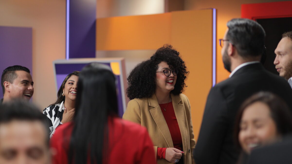 Jenny Bastidas, periodista cultural de AHORA, vestida de blazer beige y camisa roja, sonriendo en el set de AHORA, junto con Yerson Caucha, Estefanía Maldonado, José Chinchilla y Miguel Porras (de izq a der).